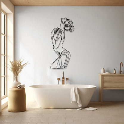 A minimalist black metal line art wall sculpture of a woman in a flowing pose, mounted on a light gray wall above a white freestanding bathtub in a bright, modern bathroom.