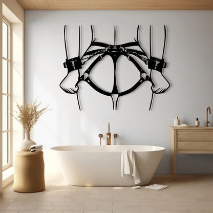 A black metal wall art piece shaped like a harness or skeletal animal structure hangs above a white freestanding bathtub in a bright, modern bathroom with wood flooring and a light wood vanity.