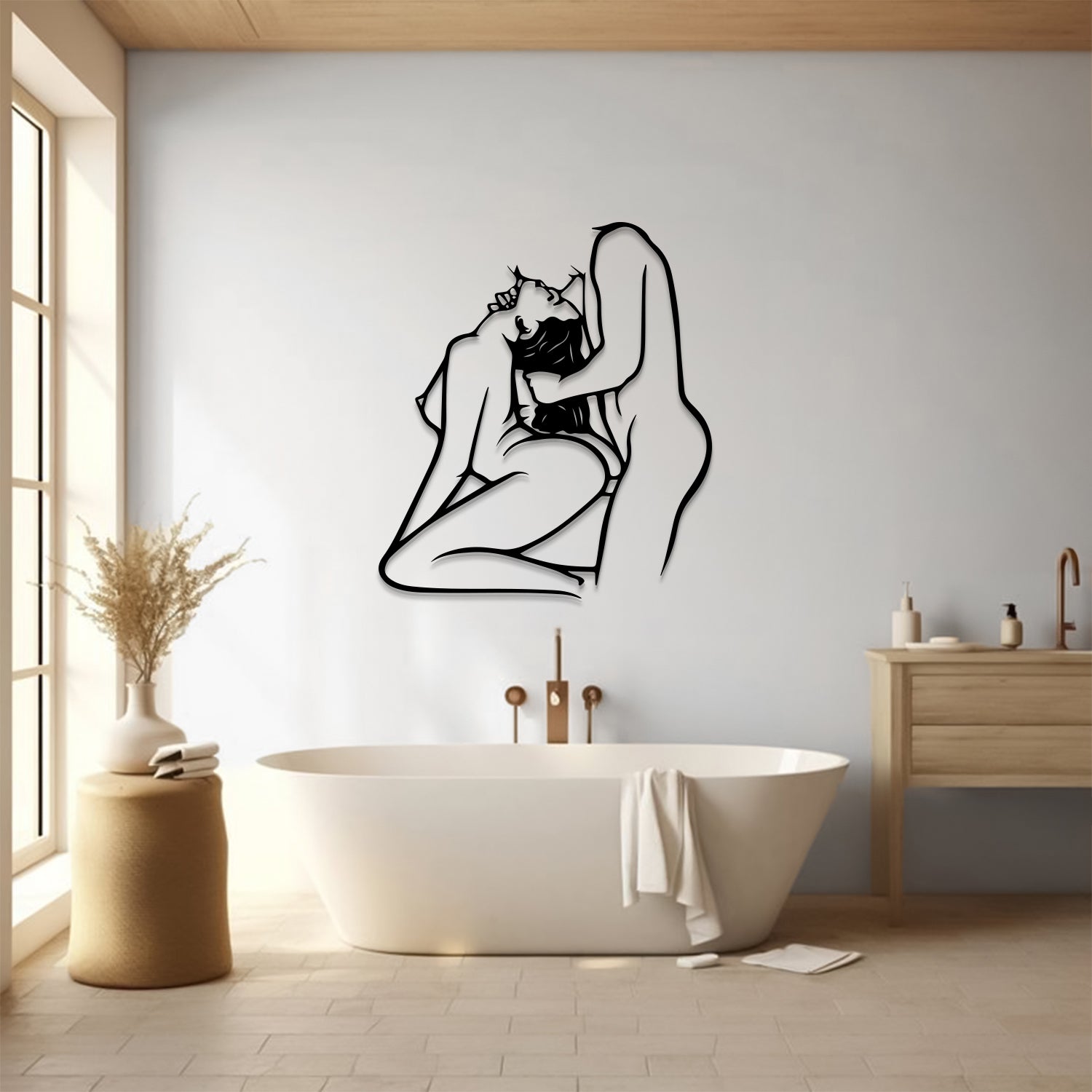 A minimalist black line art wall decal of an embracing couple is displayed on a light gray wall in a modern bathroom setting with a freestanding bathtub, wooden vanity, and warm natural light.