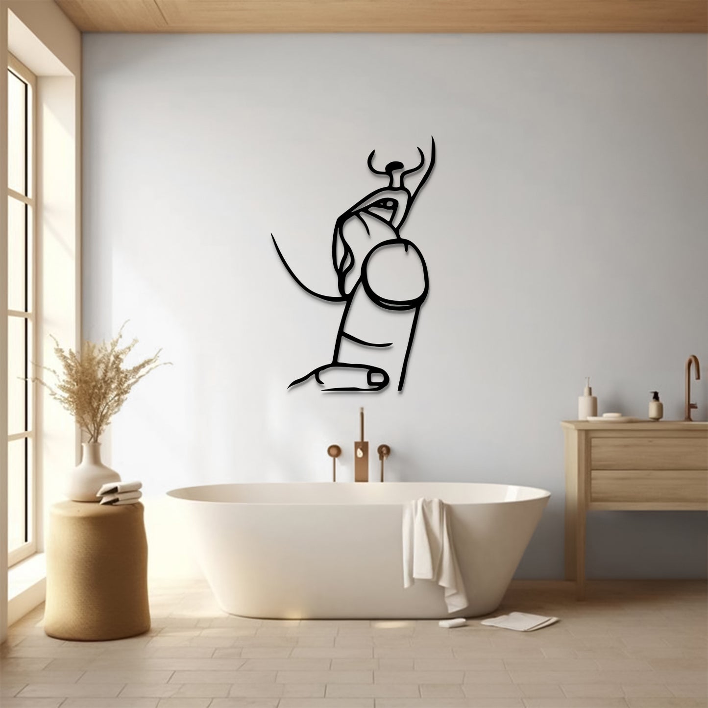 A minimalist black metal wall art piece depicting a stylized seated figure with horns, mounted on a light gray wall in a modern bathroom setting with a freestanding bathtub and wooden vanity.