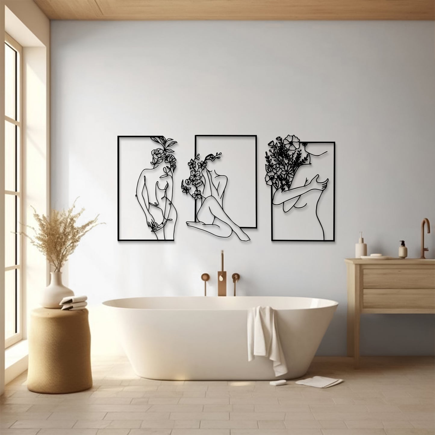 Three framed black line-art wall art prints depicting abstract female figures are displayed on a light gray wall above a white freestanding bathtub in a bright, modern bathroom.