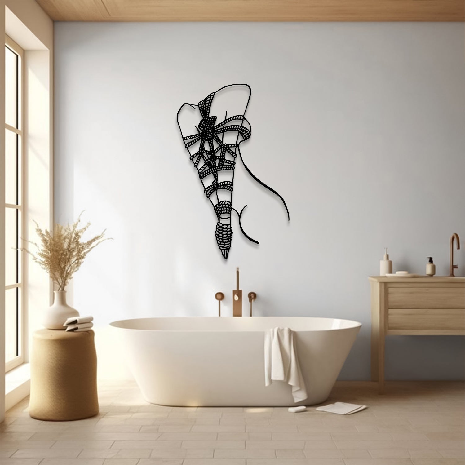 A black metal wall art sculpture of a stylized female figure hangs on a light gray wall above a white freestanding bathtub in a modern, sunlit bathroom.