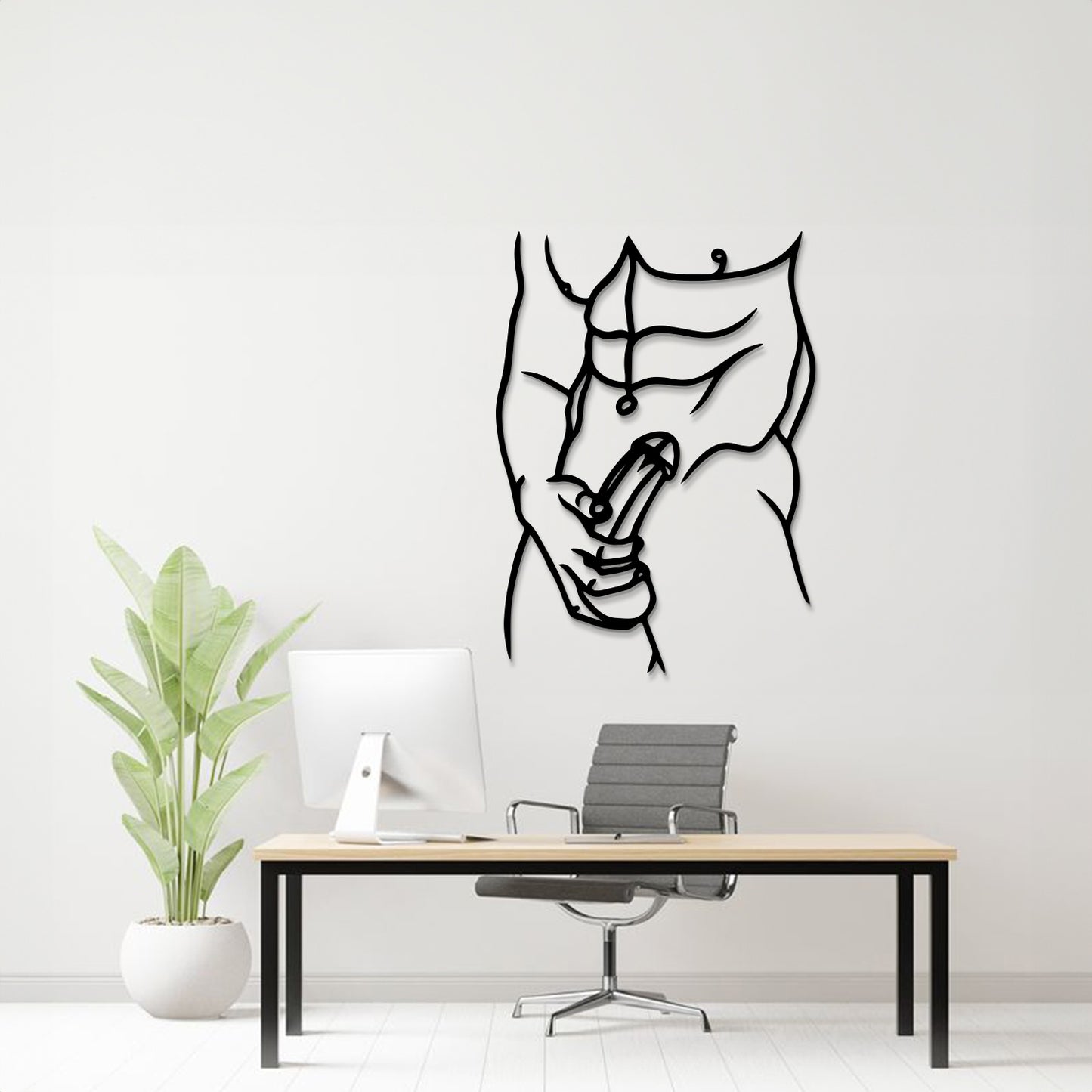 A minimalist black metal wall art piece depicting a muscular torso and hand holding a penis, displayed on a white wall above a modern desk setup with a computer, chair, and potted plant.