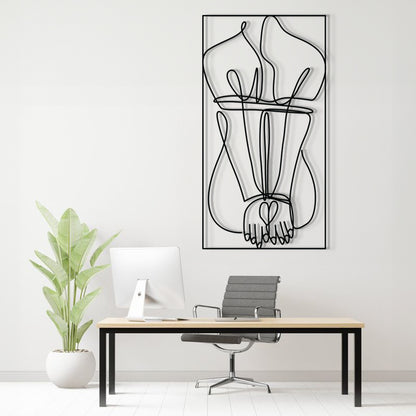 A minimalist black and white continuous line art print of hands holding hearts, displayed on a white wall above a modern desk setup with a plant and office chair.