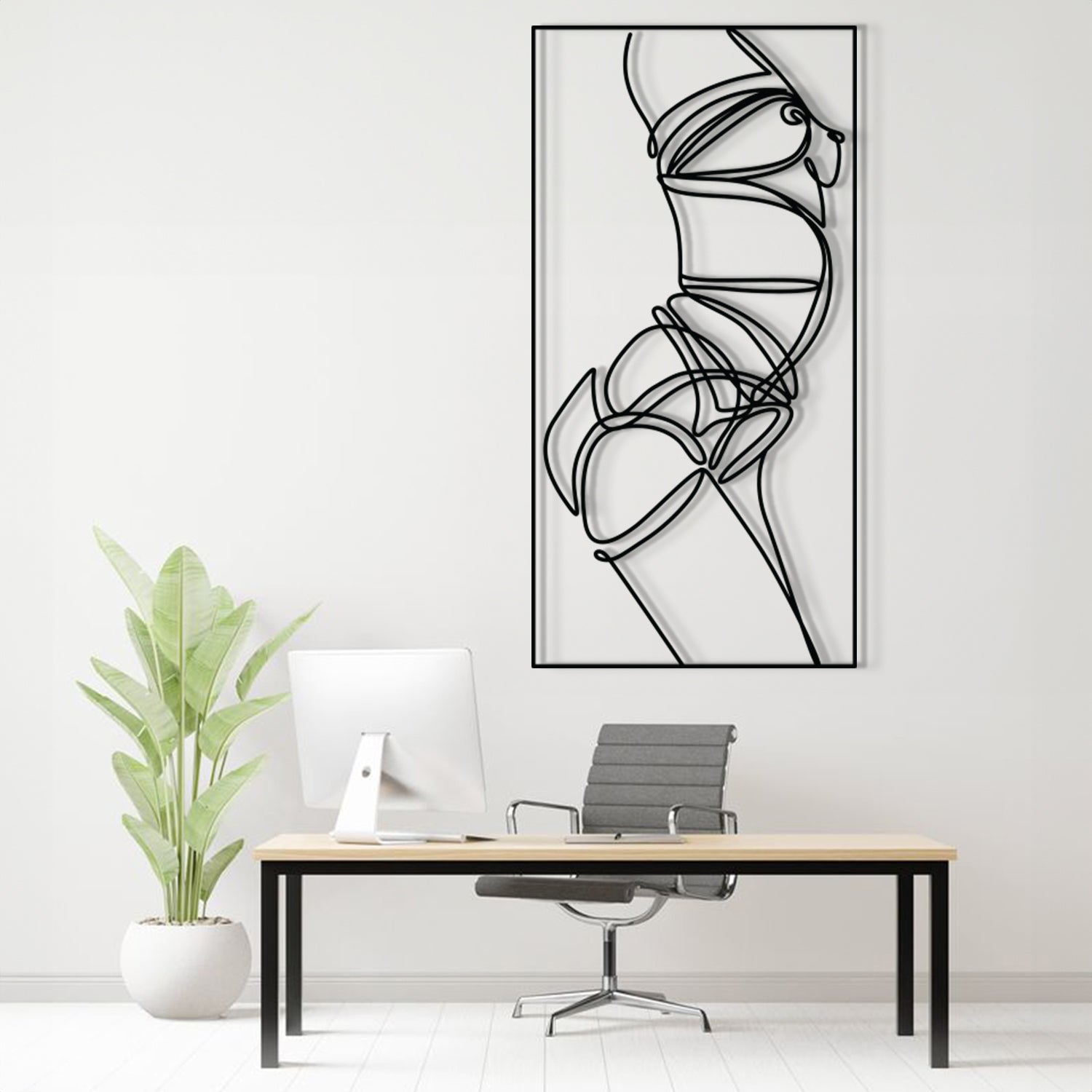 A minimalist black and white abstract line art print of a female torso is displayed on a white wall in a modern home office setting above a desk with a computer, chair, and a potted plant.