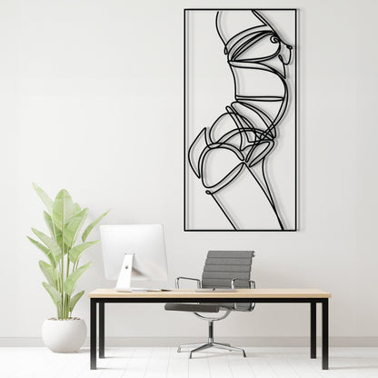 A minimalist black and white abstract line art print of a female torso is displayed on a white wall in a modern home office setting above a desk with a computer, chair, and a potted plant.
