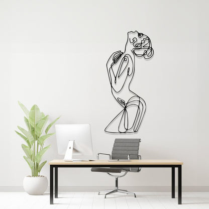 A minimalist black metal line art wall sculpture of a woman in a flowing dress, mounted on a white wall above a modern desk setup with a computer, chair, and potted plant.
