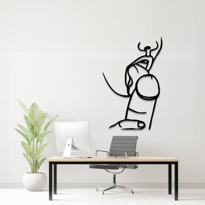A minimalist black line art wall decal of a seated figure with horns, displayed on a light gray wall above a modern desk setup with a computer, chair, and potted plant.