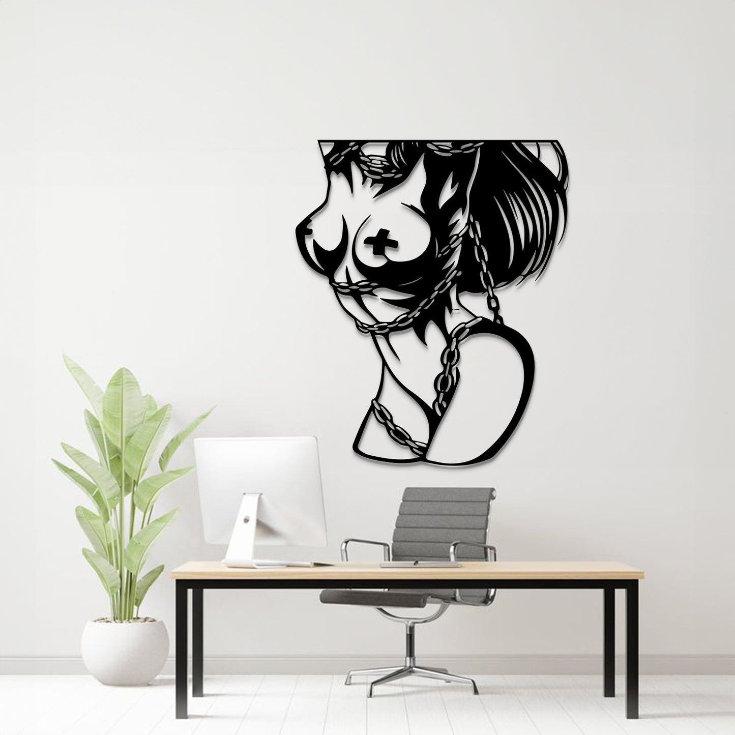 A black metal wall art piece depicting a stylized female profile with a cross on her breast and a heart-shaped chain motif, displayed on a white wall above a modern desk setup with a computer, chair, and potted plant.