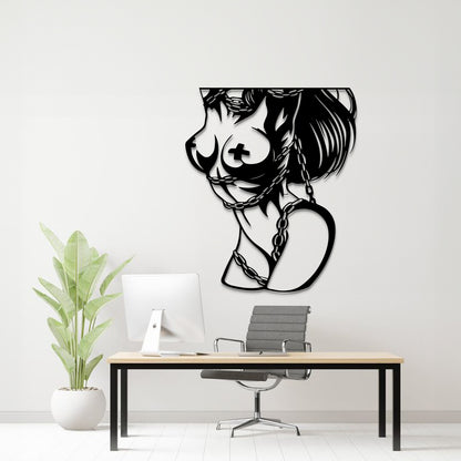 A black metal wall art piece depicting a stylized female profile with a cross on her breast and a heart-shaped chain motif, displayed on a white wall above a modern desk setup with a computer, chair, and potted plant.