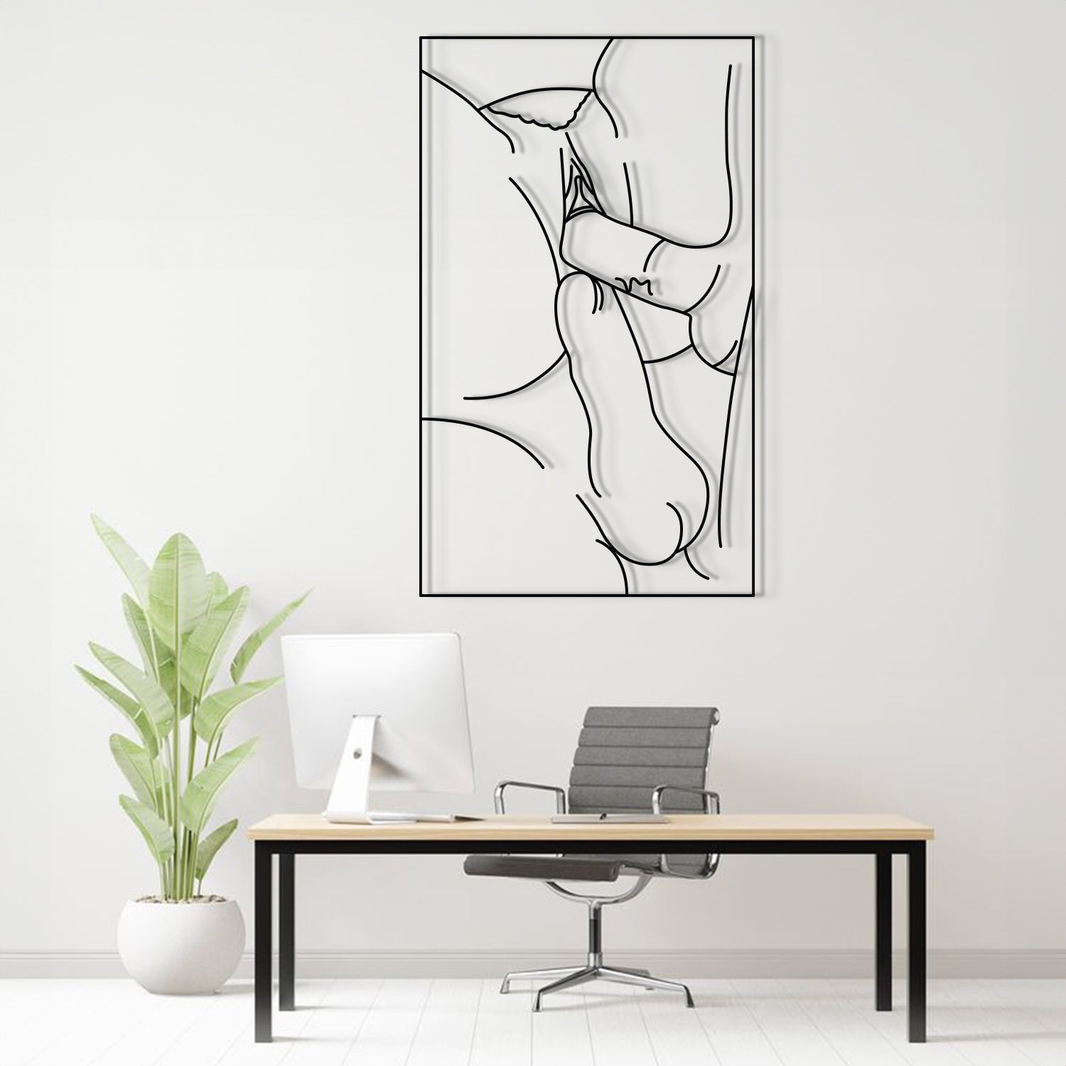 A minimalist black and white continuous line art print of a crouching figure, displayed on a white wall above a modern desk setup with a computer, chair, and potted plant.