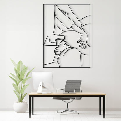 A minimalist black and white continuous line art print of a massage or touch-up scene, displayed on a light gray wall above a modern desk setup with a computer, office chair, and a potted plant.
