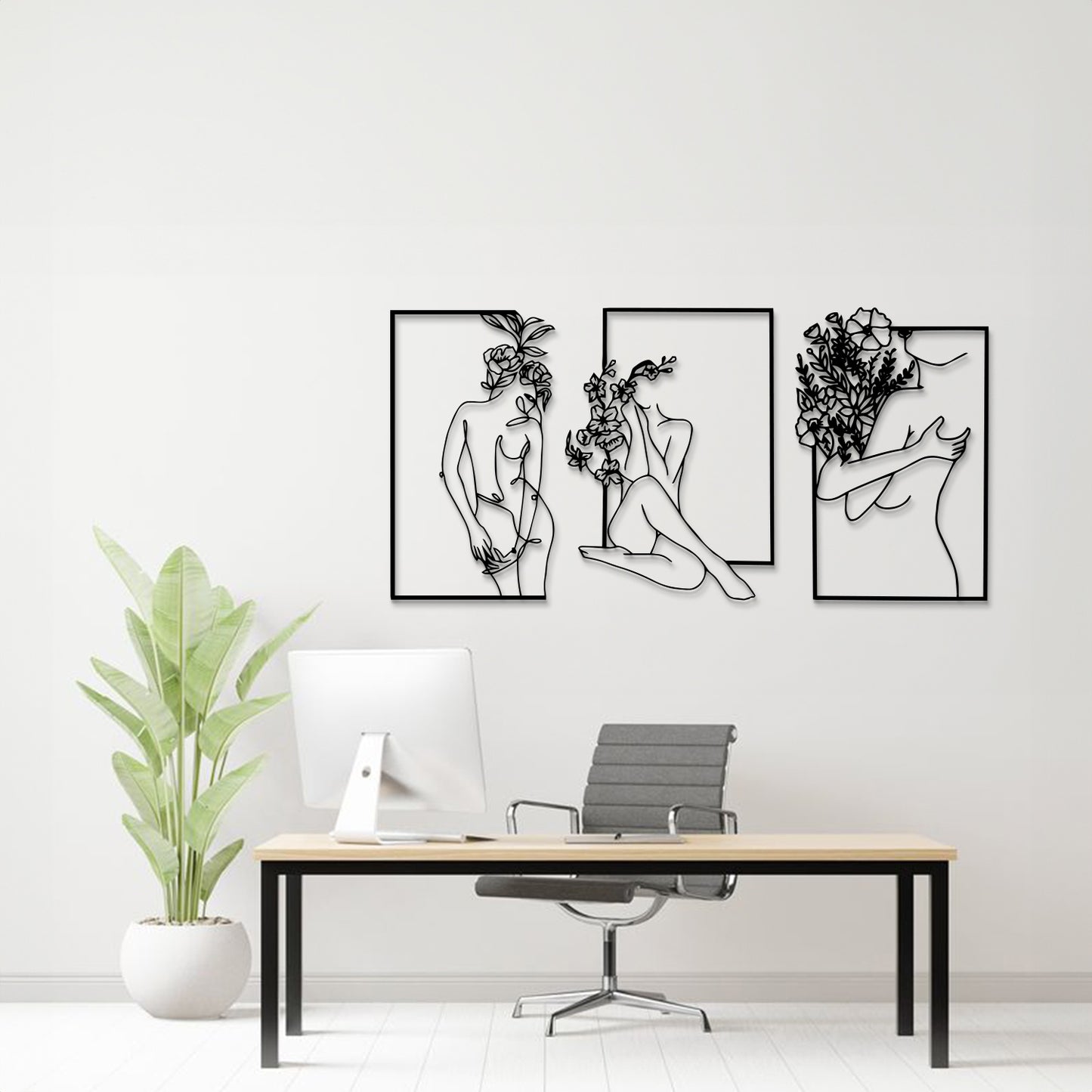Three-piece black and white metal wall art set featuring minimalist line art of women with flowers, displayed on a white wall above a modern desk setup with a plant.