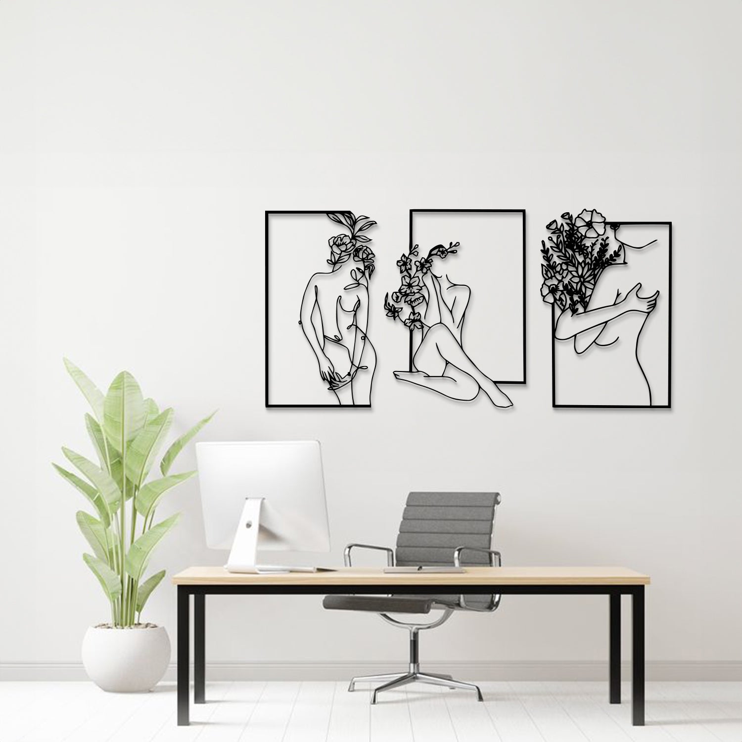 Three-piece black and white metal wall art set featuring minimalist line art of women with flowers, displayed on a white wall above a modern desk setup with a plant.