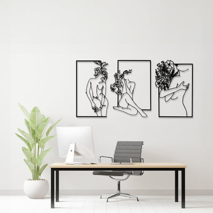 Three-piece black and white metal wall art set featuring minimalist line art of women with flowers, displayed on a white wall above a modern desk setup with a plant.