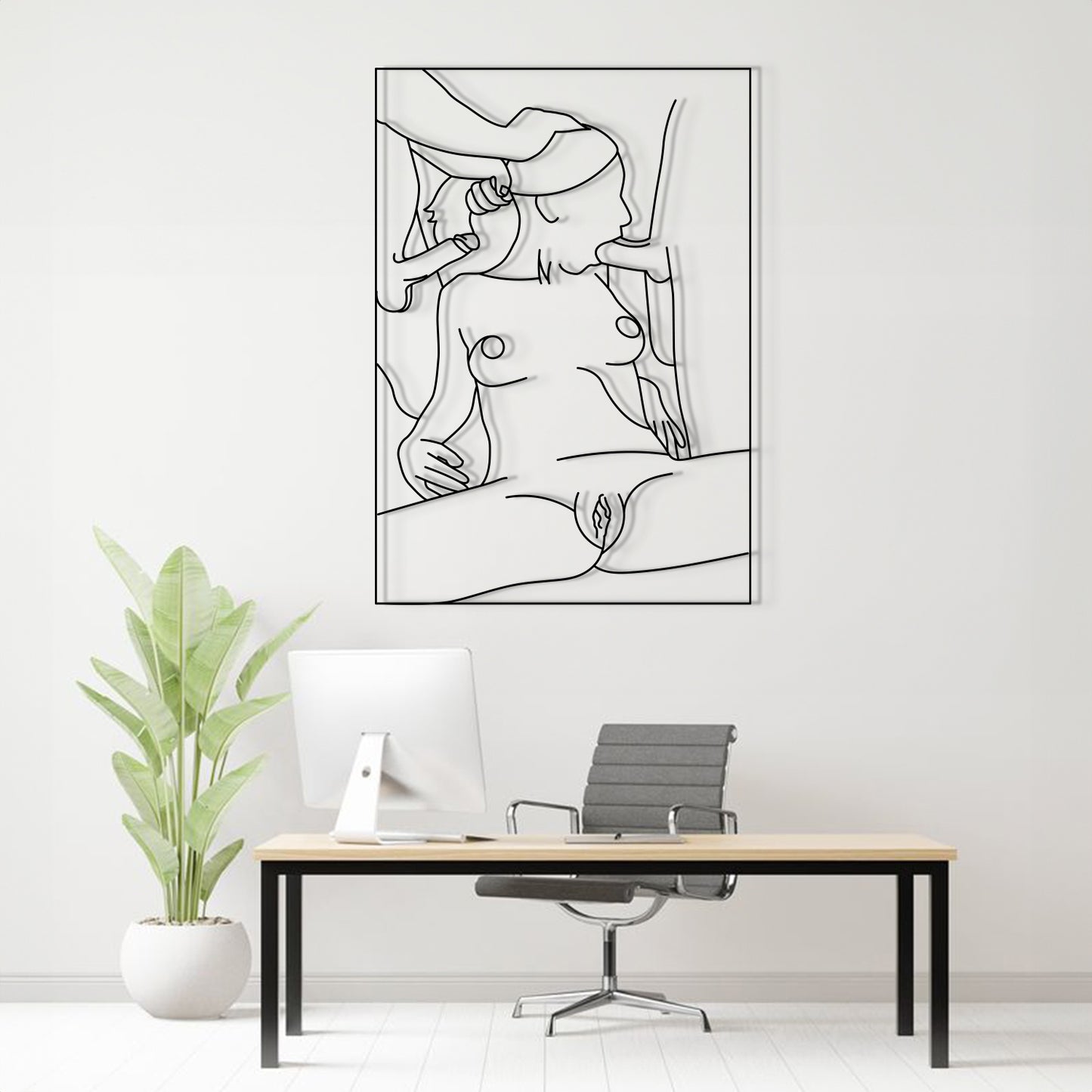 A minimalist black and white continuous line art print of a nude female figure is displayed on a white wall above a modern desk setup with a computer, chair, and a potted plant.