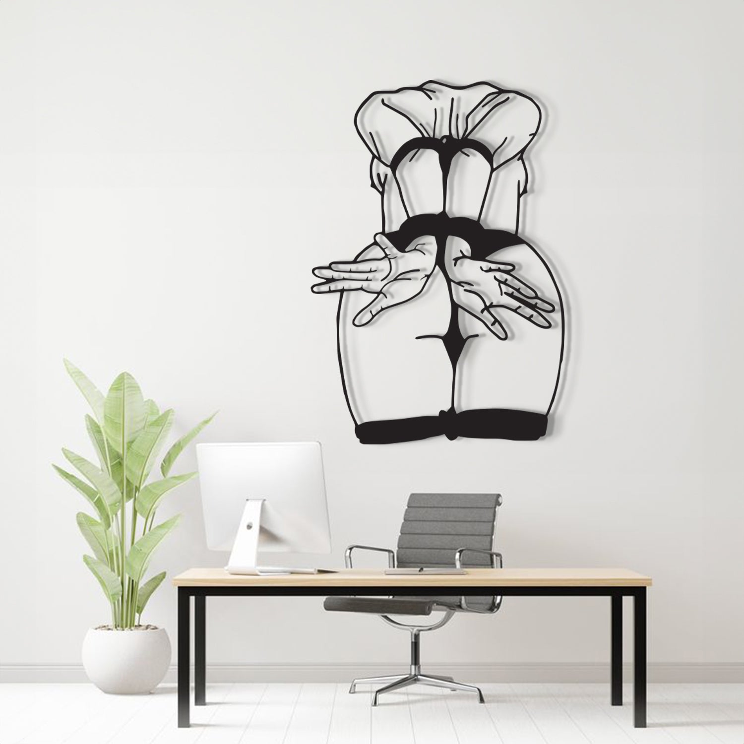 A black and white line art wall decal depicting a stylized female figure from behind, displayed on a light gray wall above a modern desk setup with a computer, chair, and potted plant.
