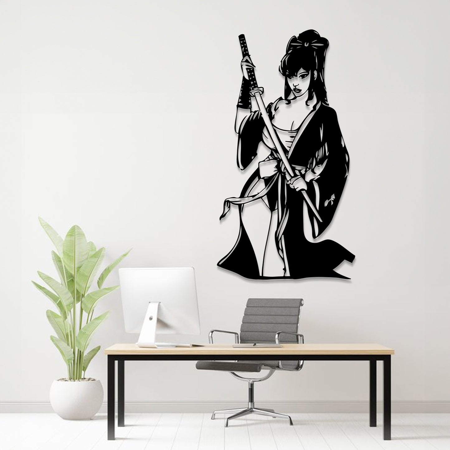 A black metal wall art piece depicting a samurai woman holding a sword, displayed on a white wall above a modern desk setup with a computer, chair, and potted plant.