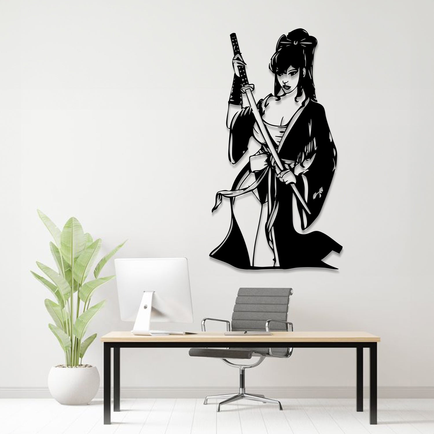 A black metal wall art piece depicting a samurai woman holding a sword, displayed on a white wall above a modern desk setup with a computer, chair, and potted plant.