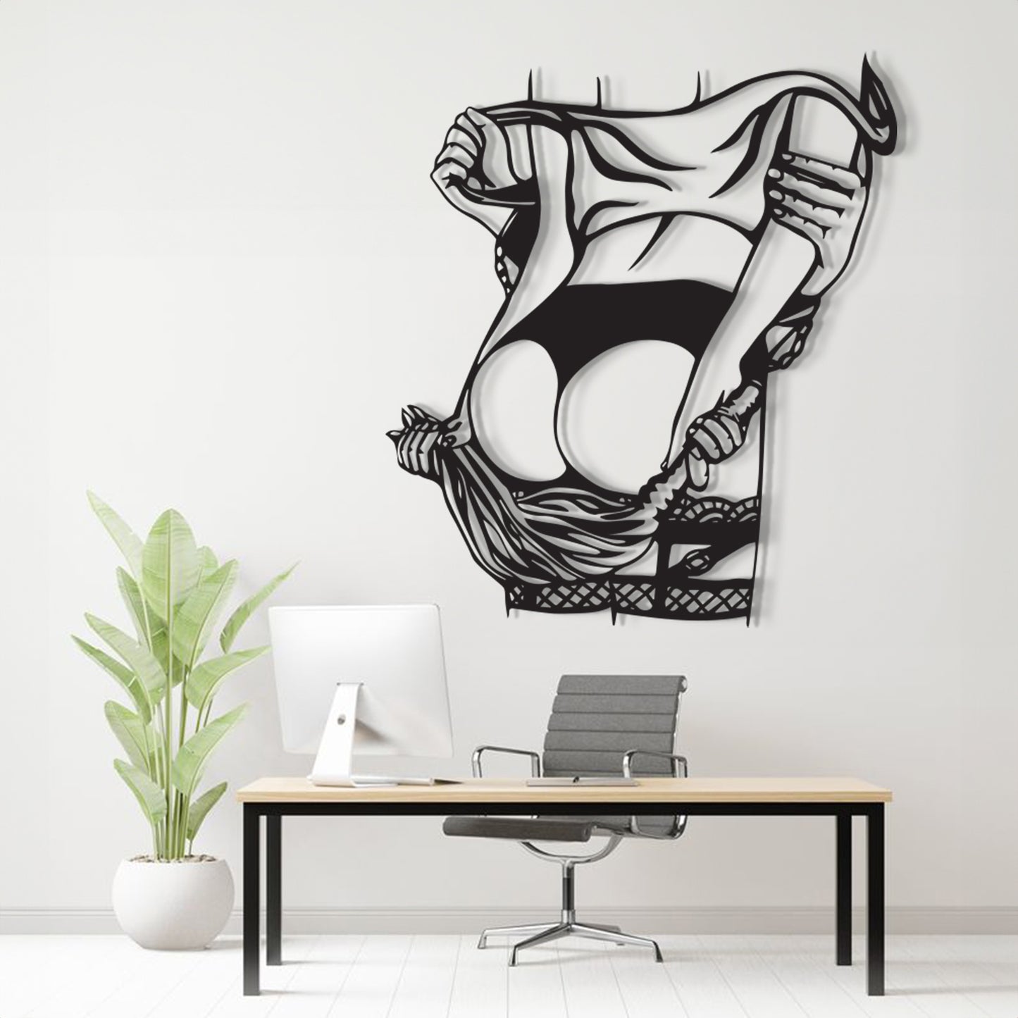 A black and white stylized wall art print of a woman lifting her skirt, displayed on a light gray wall above a modern desk setup with a computer, chair, and potted plant.