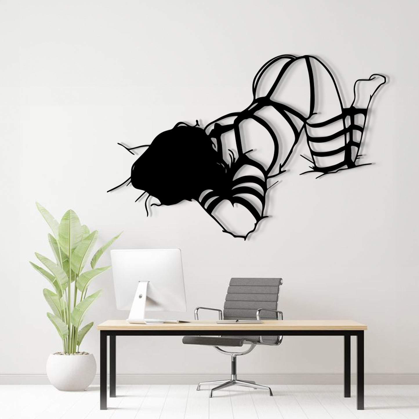 A black metal wall art sculpture of a woman in a bikini floating on her knees, displayed above a modern desk setup in a bright, minimalist office room.