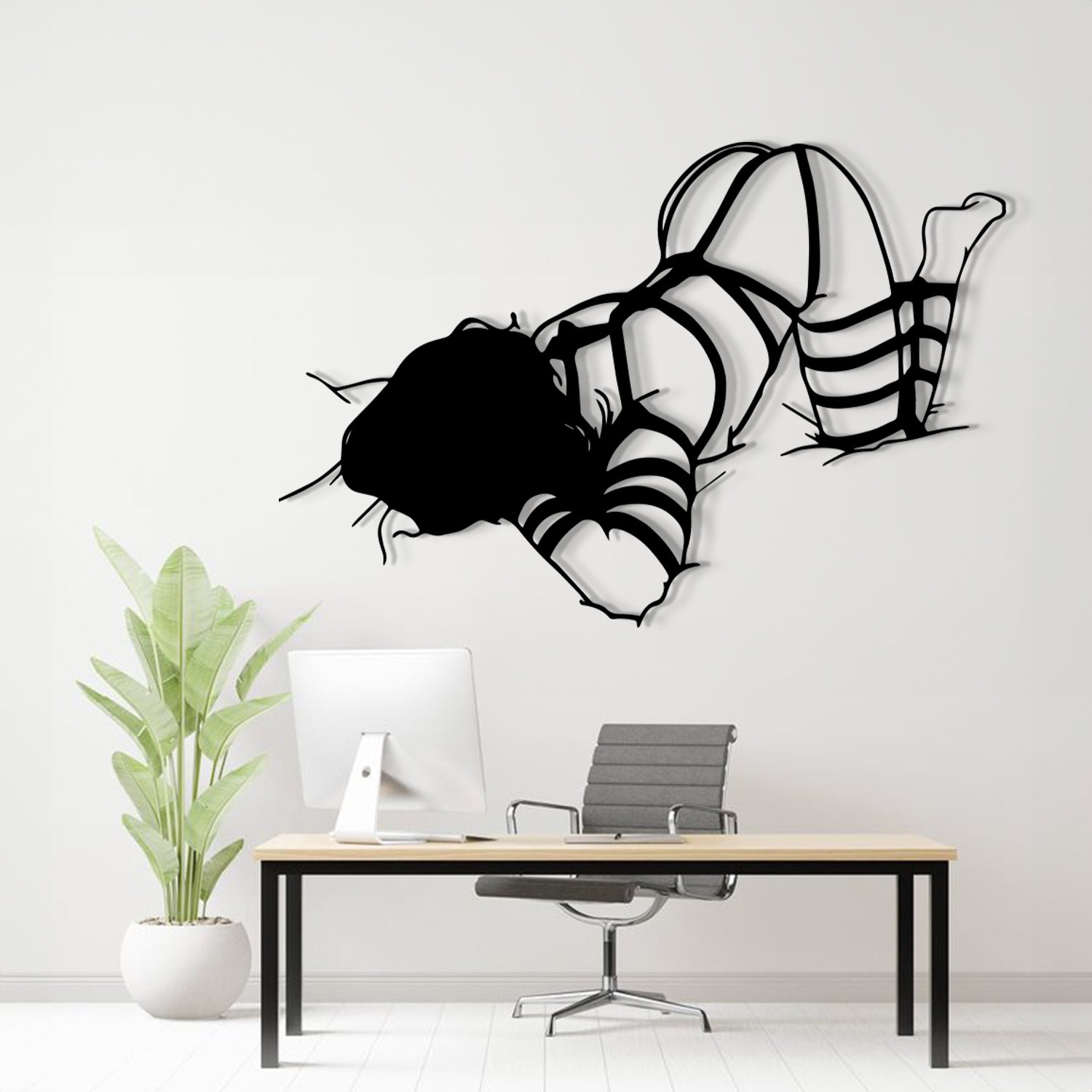 A black metal wall art sculpture of a woman in a bikini floating on her knees, displayed above a modern desk setup in a bright, minimalist office room.