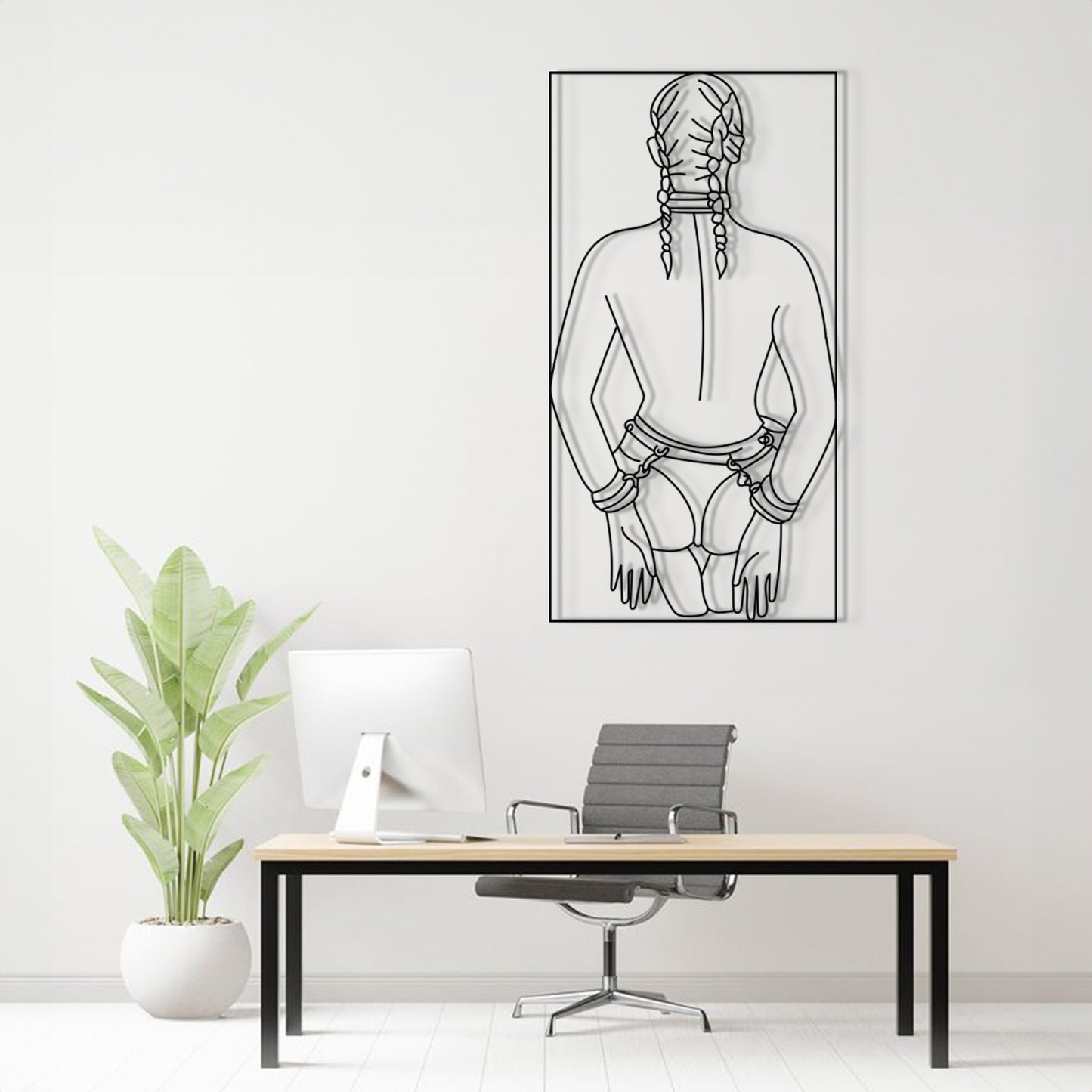 A minimalist black and white line art poster of a woman's back with braids, displayed on a white wall above a modern desk setup with a computer, chair, and potted plant.