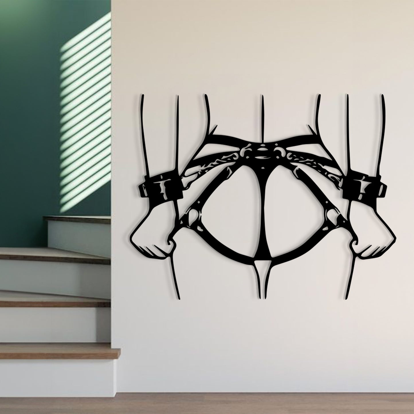 Black metal wall art depicting a stylized torso and arms with chains, mounted on a white wall in a modern interior setting next to a staircase.