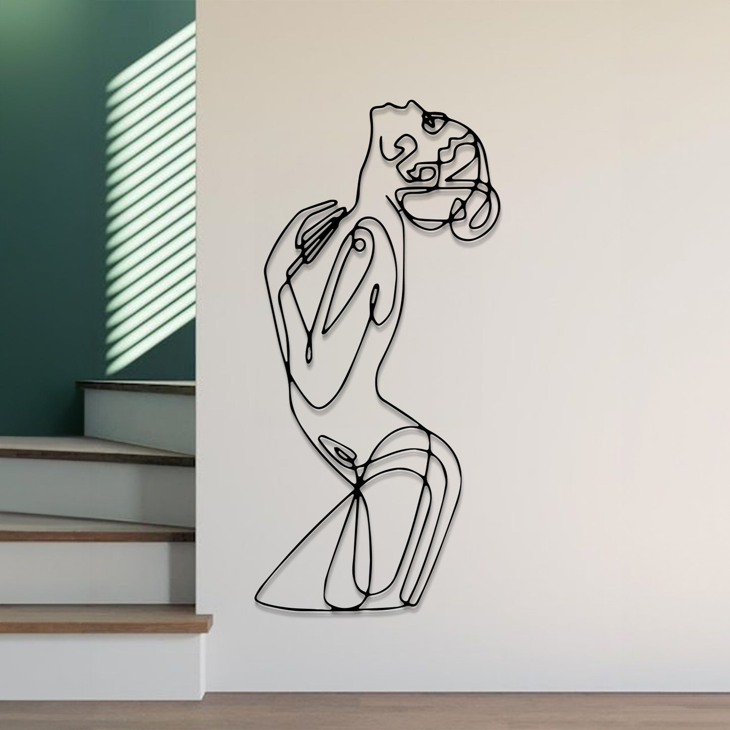Abstract black line art wall sculpture of a dancing woman, mounted on a white wall in a modern interior setting with stairs and a green accent wall visible.