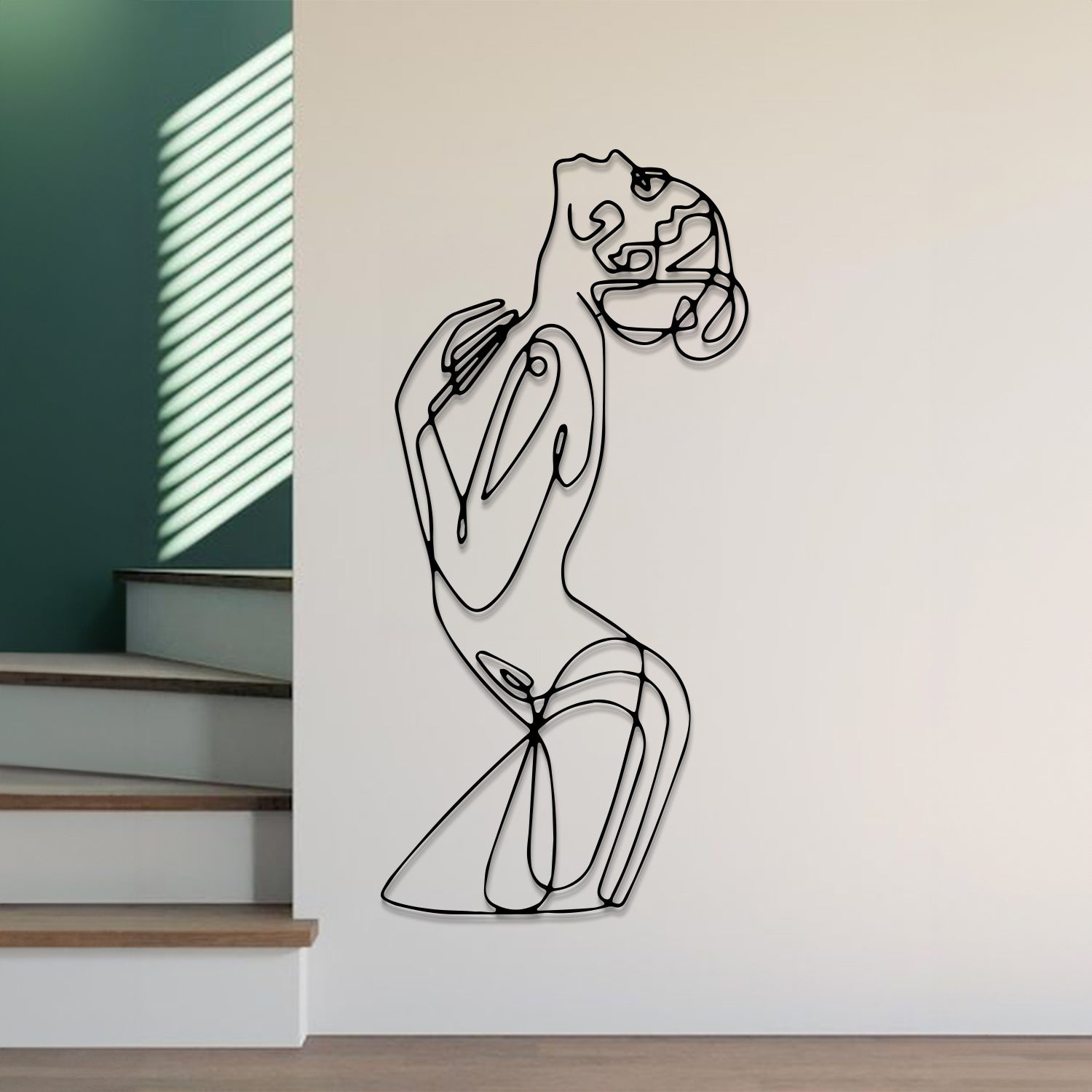 Abstract black line art wall sculpture of a dancing woman, mounted on a white wall in a modern interior setting with stairs and a green accent wall visible.