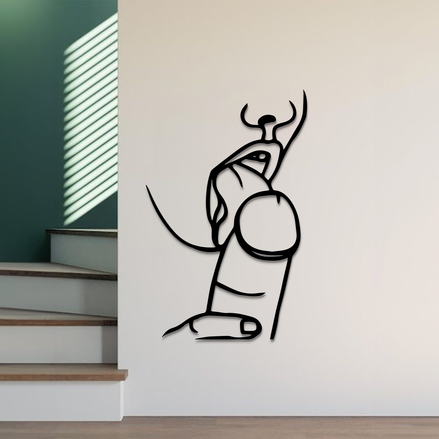 A minimalist black metal wall art piece depicting a stylized figure, mounted on a white wall in a modern interior setting with stairs and window blinds visible.