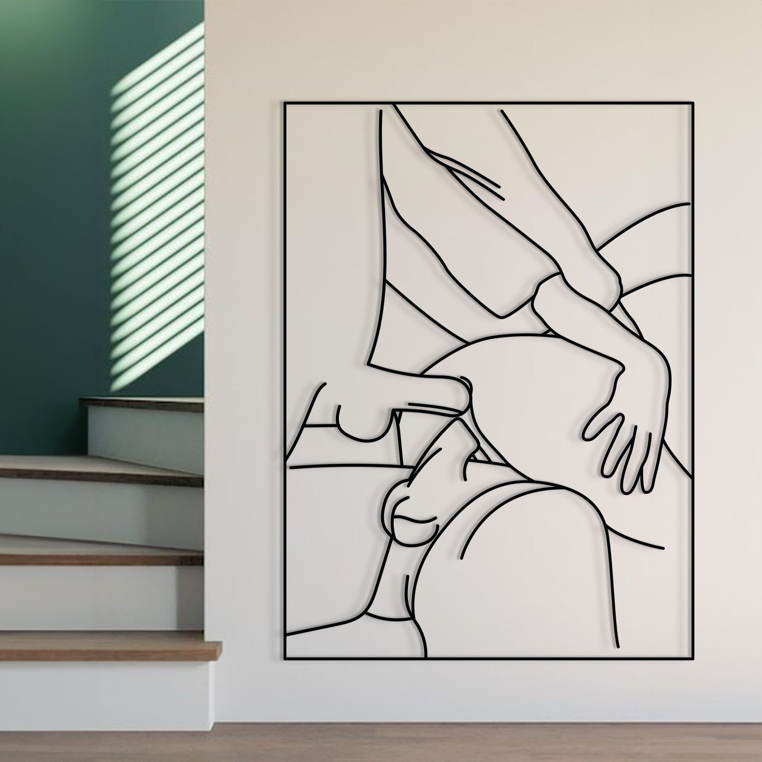 A minimalist black and white line art poster depicting an intimate embrace, displayed on a light beige wall in a modern interior setting next to a staircase.