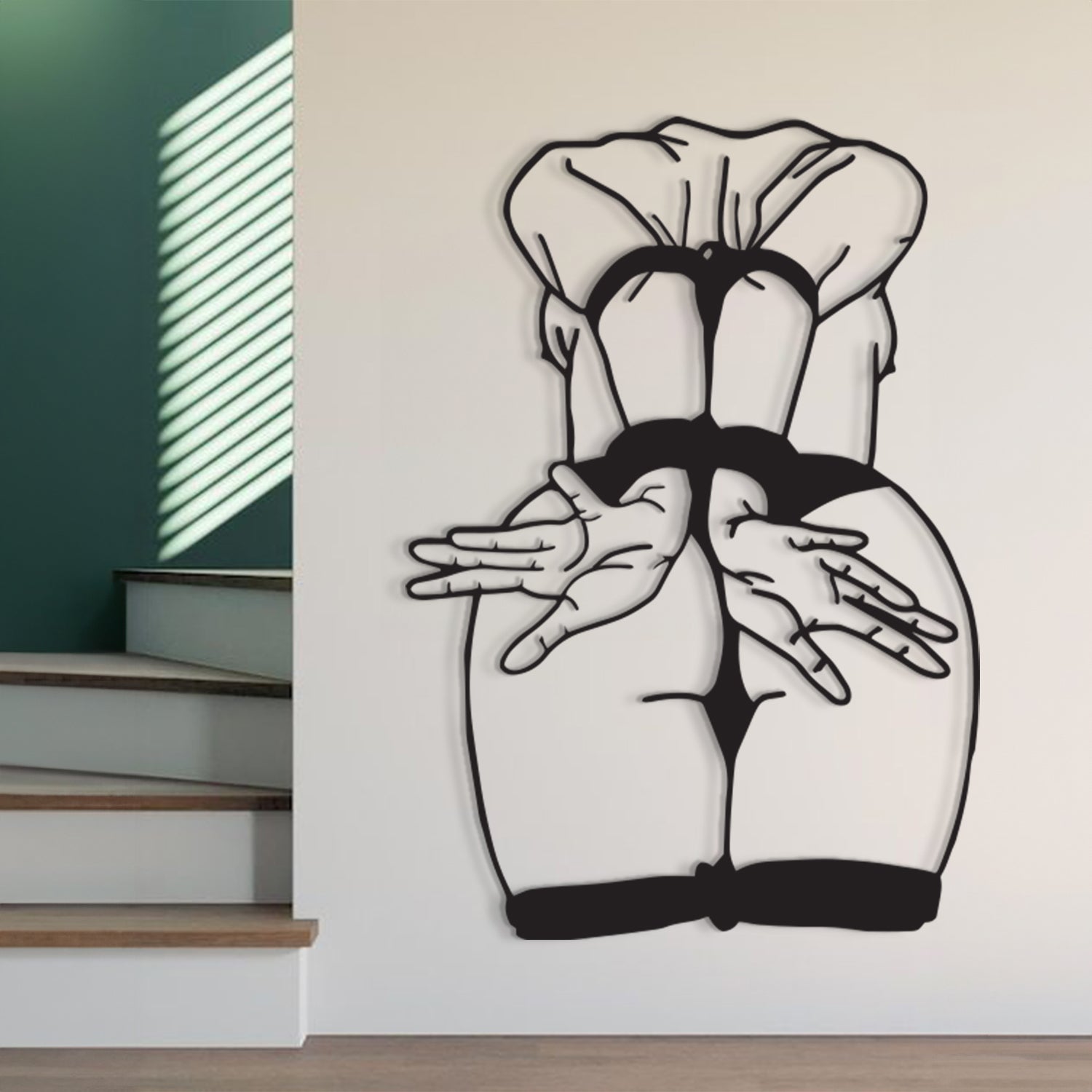 Black and white wall art depicting a stylized rear view of a person in a ruffled top and black underwear, mounted on a white wall in a modern interior setting with stairs and window blinds visible.