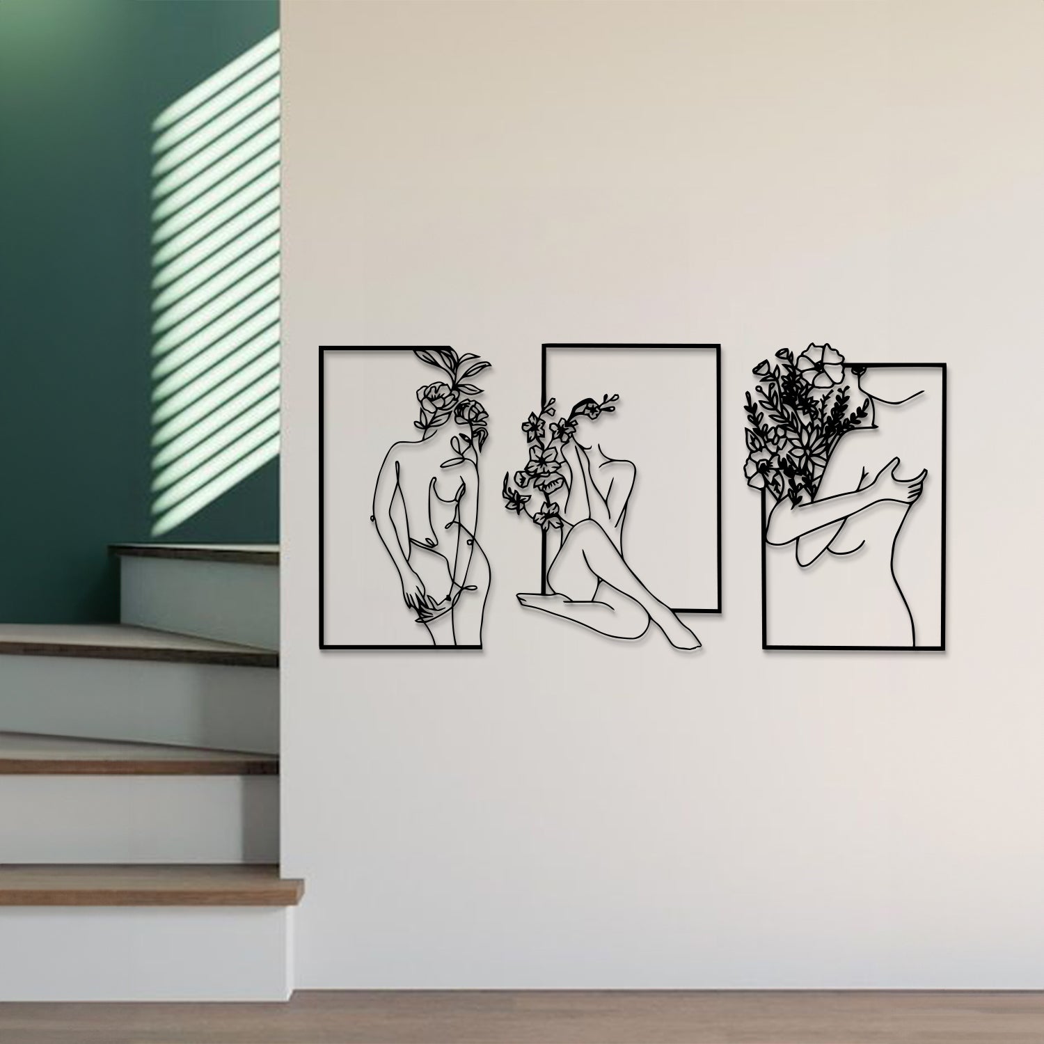 Three-piece black metal wall art set featuring minimalist line drawings of female figures and floral motifs, displayed on a white wall in a modern interior setting.