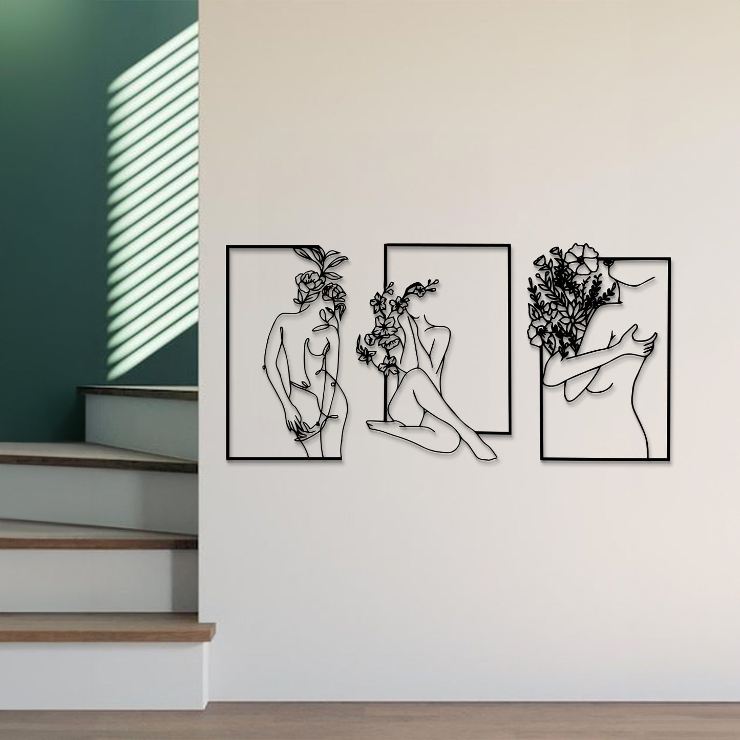 Three-piece black metal wall art set featuring minimalist line drawings of female figures and floral motifs, displayed on a white wall in a modern interior setting.