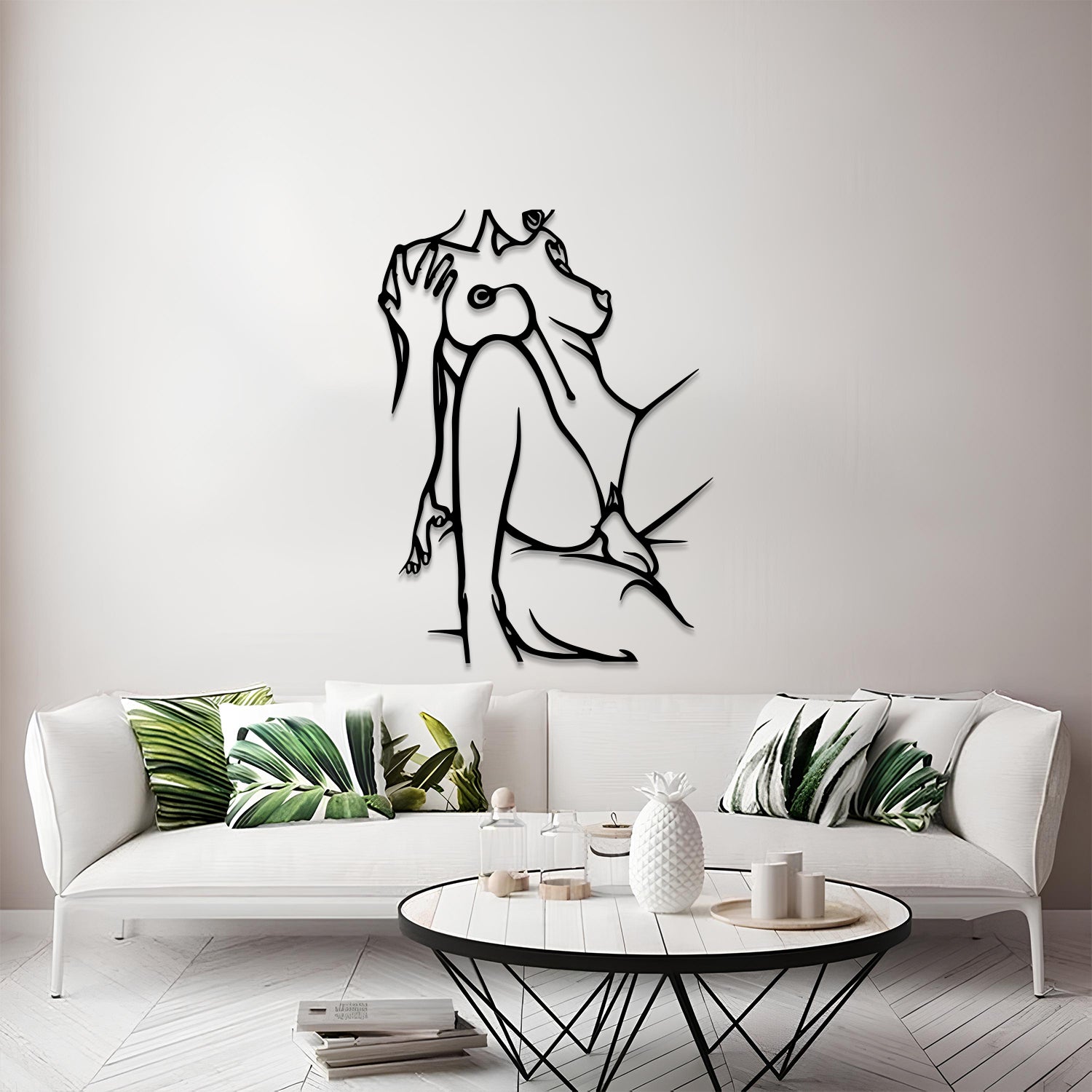 A modern living room scene featuring a black metal wall art piece of a seated figure in profile mounted on a light gray wall above a white sofa with green leaf-patterned pillows.