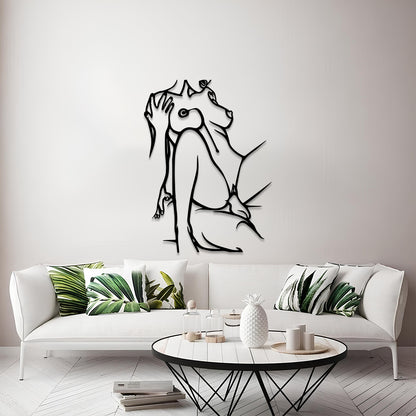 A modern living room scene featuring a black metal wall art piece of a seated figure in profile mounted on a light gray wall above a white sofa with green leaf-patterned pillows.