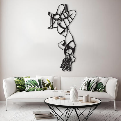 A modern living room scene featuring a white sofa with green tropical leaf patterned throw pillows, a round black coffee table, and a tall black metal abstract wall sculpture mounted on a light gray wall.