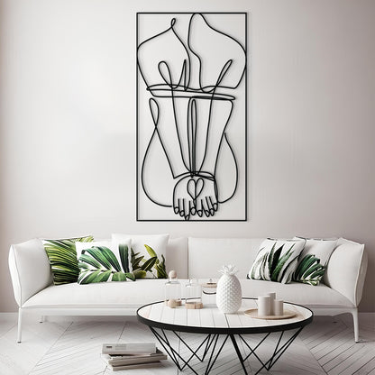 A modern living room scene featuring a large black wire art piece of intertwined hands hanging on a light gray wall above a white sofa with green leaf-patterned pillows.