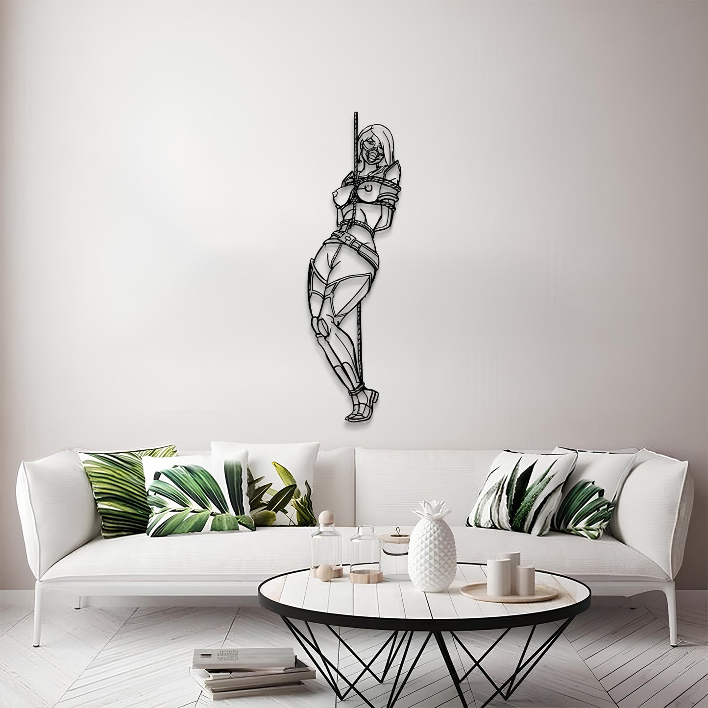 A black metal wall art piece depicting a stylized, geometric female figure hanging from a pole, displayed on a light gray wall above a modern white sofa with green leaf-patterned pillows.