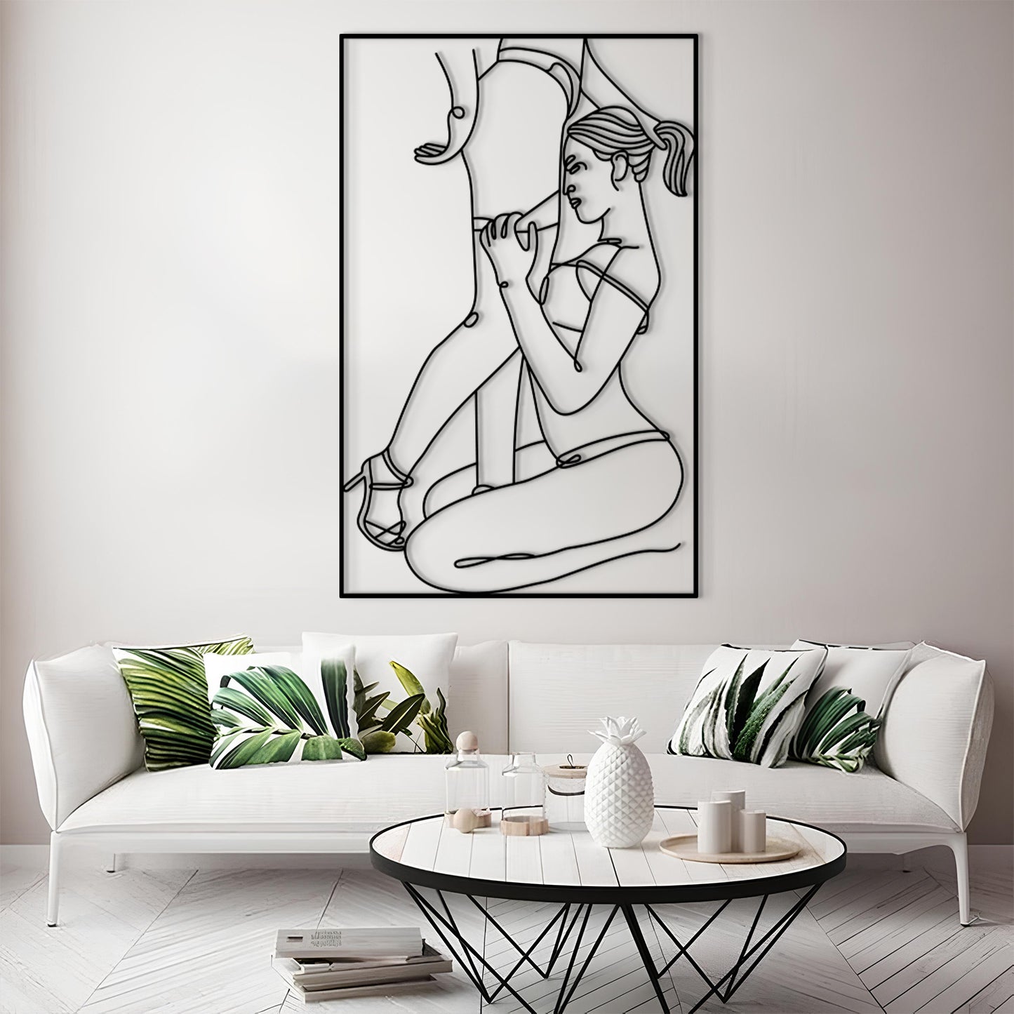 A framed black and white minimalist line art print of a woman is displayed on a light gray wall above a white sofa with green leaf-patterned pillows in a modern living room setting.