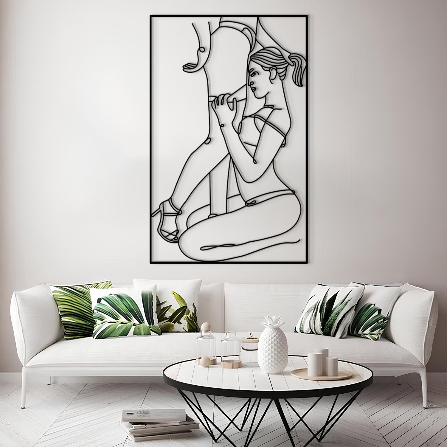 A framed black and white minimalist line art print of a woman is displayed on a light gray wall above a white sofa with green leaf-patterned pillows in a modern living room setting.
