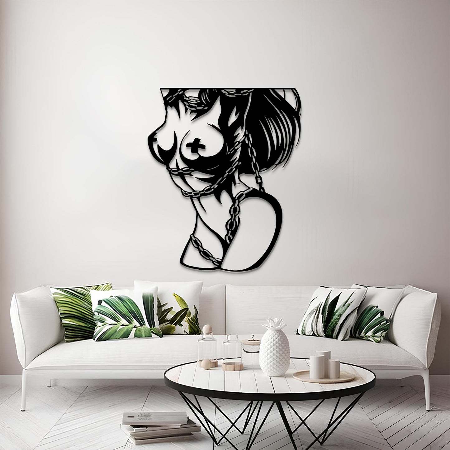A black metal wall art piece depicting a stylized female profile with a cross motif on the breast and a heart-shaped pendant, displayed on a light gray wall above a white sofa in a modern living room setting.