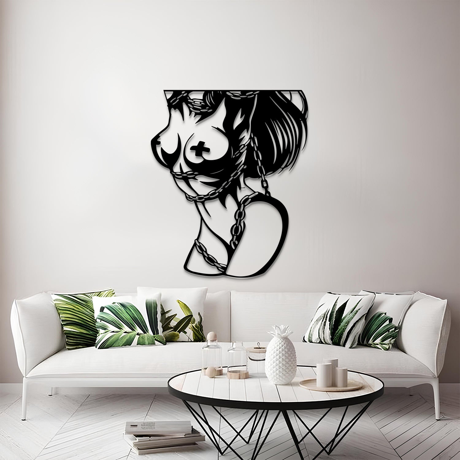 A black metal wall art piece depicting a stylized female profile with a cross motif on the breast and a heart-shaped pendant, displayed on a light gray wall above a white sofa in a modern living room setting.