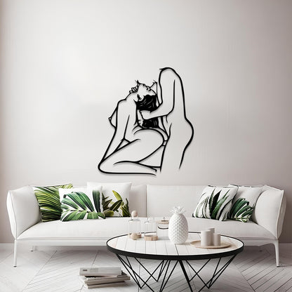 A black metal wall art piece depicting a minimalist line drawing of a kissing couple, mounted on a light gray wall above a modern white sofa with green leaf-patterned pillows.