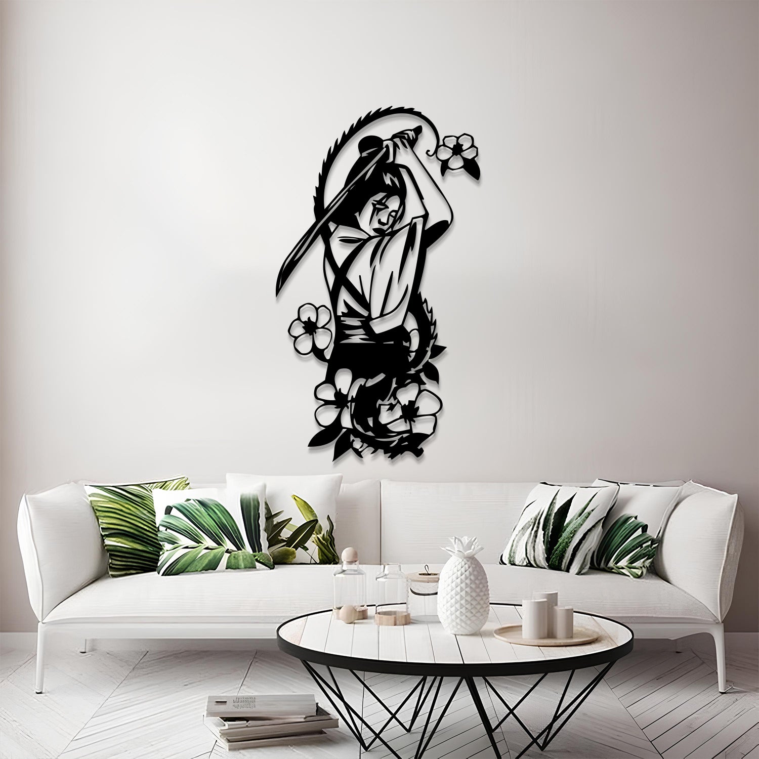 A black metal wall art piece depicting a samurai warrior with a sword and surrounding flowers, mounted on a light gray wall above a modern white sofa with green leaf-patterned pillows.