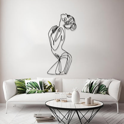 A modern minimalist living room featuring a black wire art piece of a stylized female figure on the wall above a white sofa with green leaf-patterned pillows.