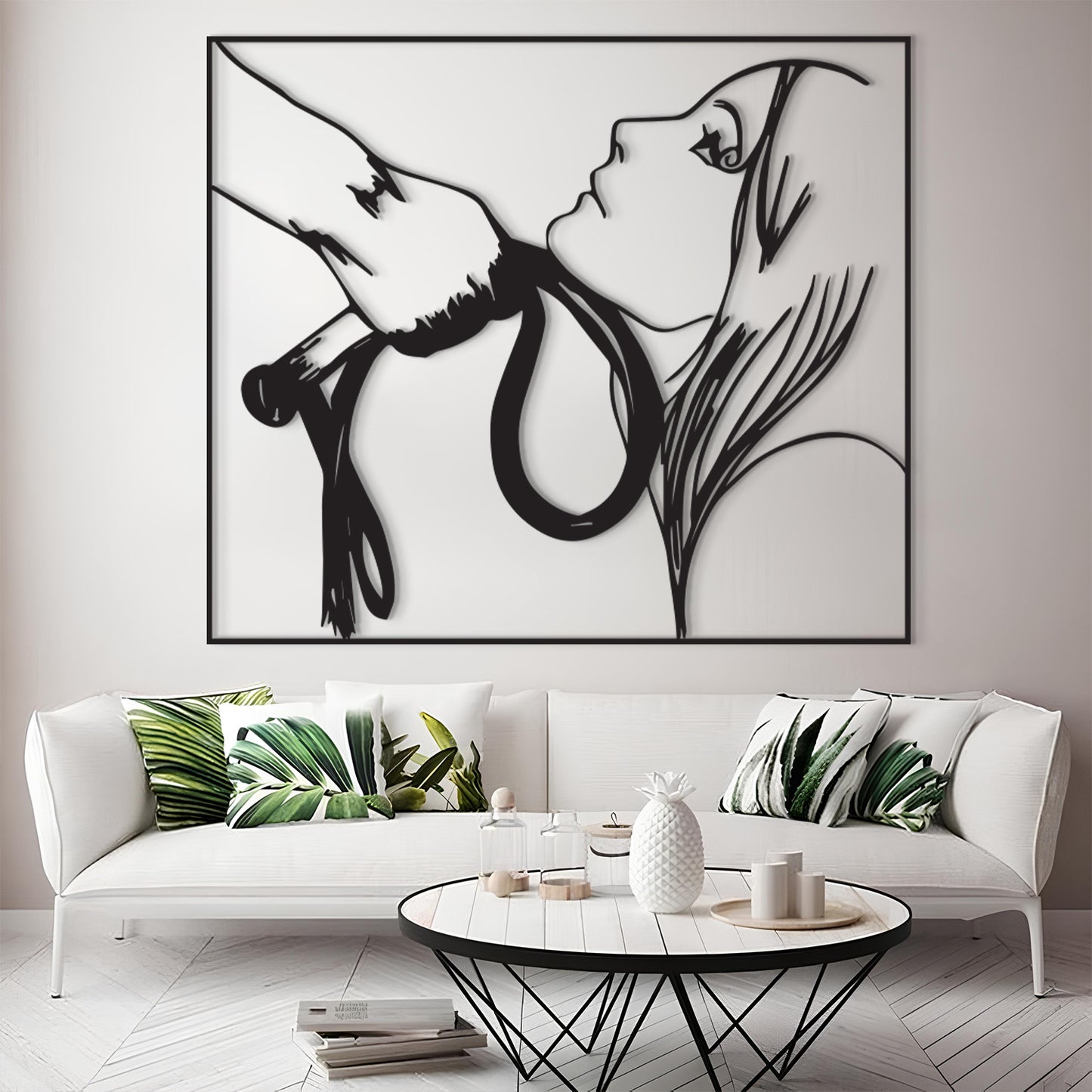 A large black and white minimalist wall art print depicting a woman's profile and a hand holding a snake, displayed above a white sofa in a modern living room setting.