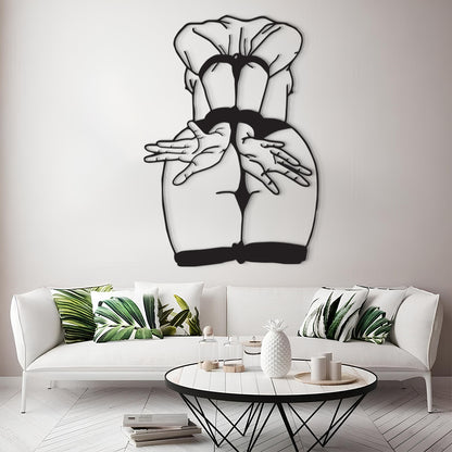 A black metal wall art piece depicting a stylized rear view of a woman in a chef's hat and black dress, displayed on a light gray wall above a modern white sofa with green leaf-patterned pillows.