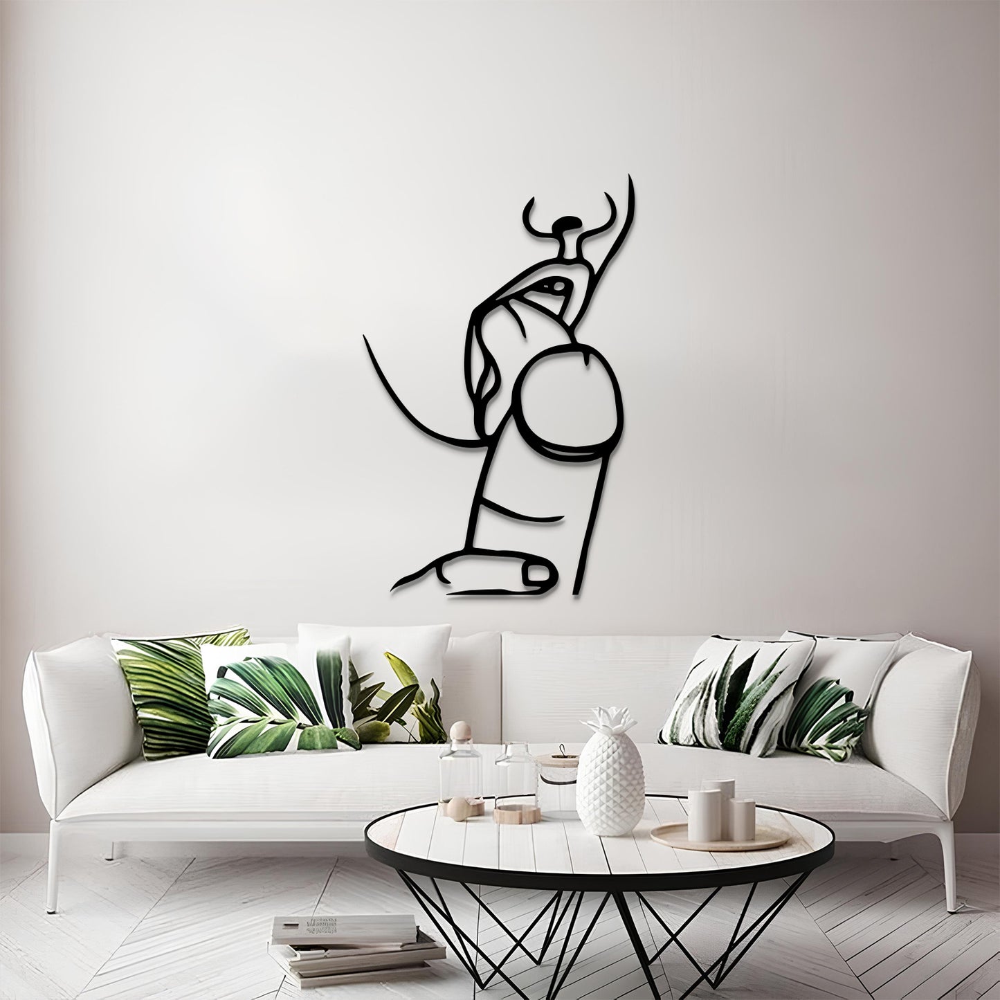 A minimalist black metal wall art piece depicting an abstract bull, displayed on a light gray wall above a modern white sofa with green leaf-patterned pillows.
